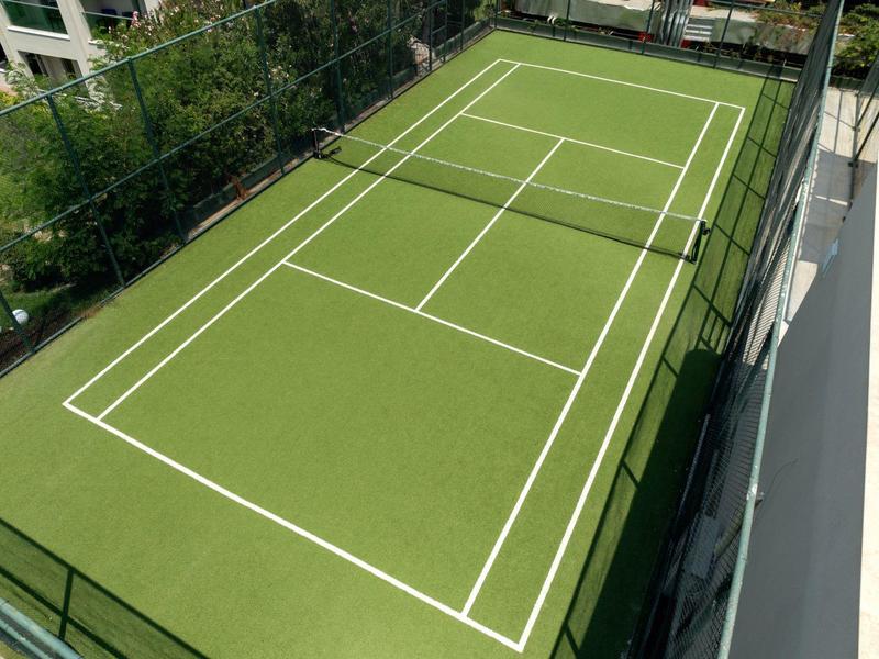 Pista de tenis verde con líneas blancas, rodeada de vallas, ideal para deportes en el hotel.