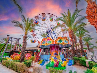 Parque de atracciones colorido con noria y palmeras al atardecer.