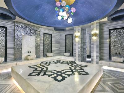 Área de bienestar moderna con hammam geométrico y suelo de mosaico decorativo bajo luz de cúpula azul.