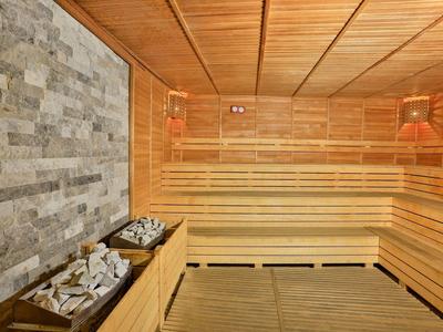 Sala de sauna con revestimiento de madera, piedras y luz cálida para relajación en hotel.