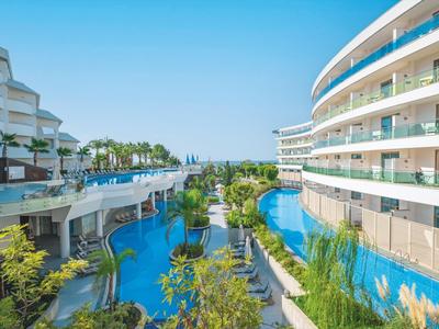 Complesso alberghiero moderno con due edifici e una grande piscina centrale, circondato da vegetazione.