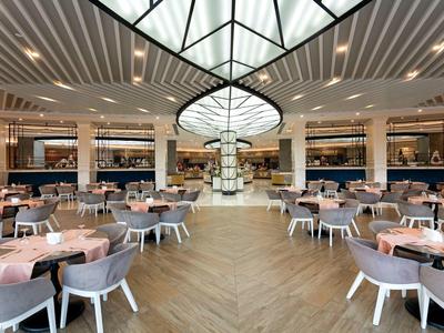 Amplio restaurante hotelero con techo moderno y mesas redondas elegantemente dispuestas.
