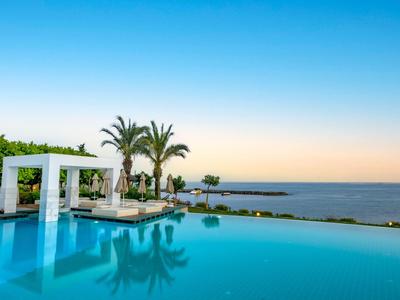 Piscina a sfioro con palme e vista mare al tramonto.
