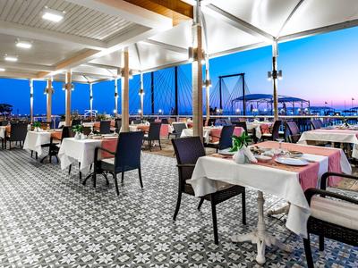 Restaurante al aire libre con mesas preparadas y vista a un puente iluminado al atardecer.