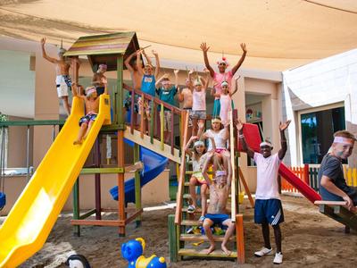 Niños felices jugando en un área de juegos cubierta colorida con tobogán y estructura para escalar.