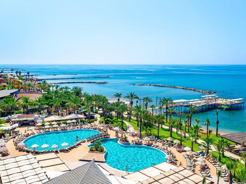 Complejo hotelero con piscinas, palmeras y acceso directo al mar bajo un cielo despejado.