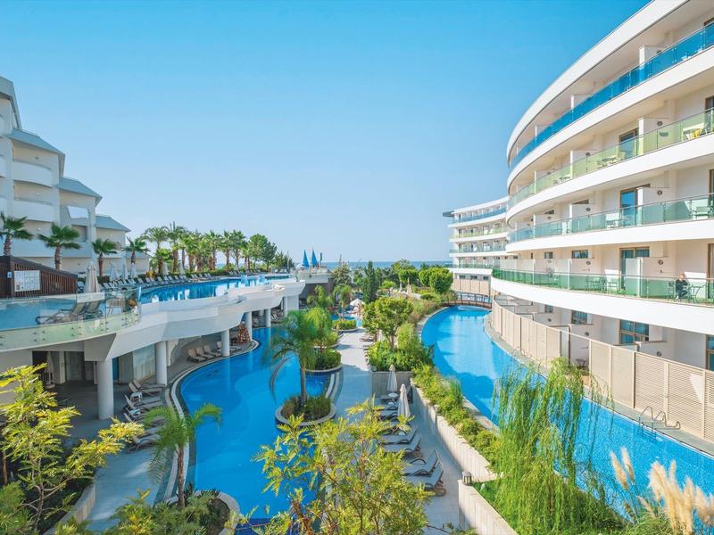 Complejo hotelero moderno con piscina y plantas verdes bajo un cielo despejado.