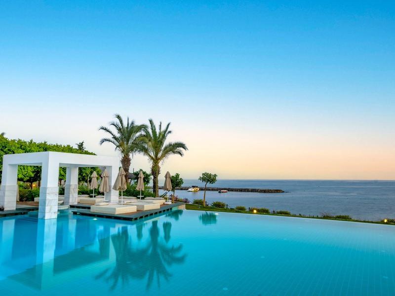 Piscina infinita con tumbonas y palmeras con vistas al mar bajo cielo despejado