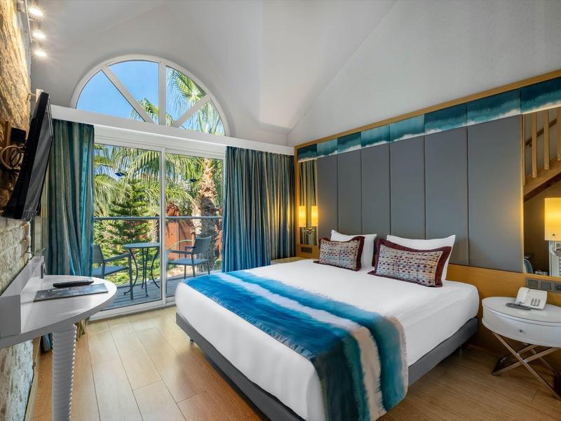 Habitación de hotel moderna con grandes ventanas y balcón, luminosa con cama doble.