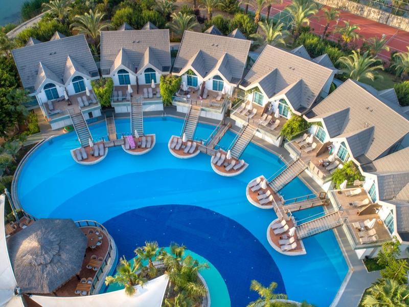 Vista aérea de un hotel semicircular con piscina y tumbonas junto al agua.