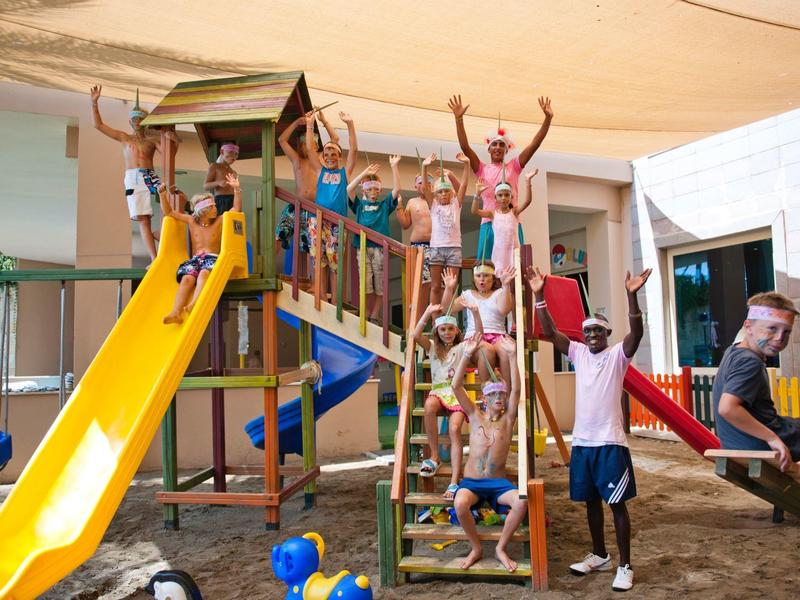 Niños felices jugando en un área de juegos cubierta colorida con tobogán y estructura para escalar.