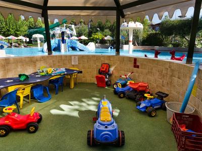 Speelruimte voor kinderen met kleine voertuigen en zitplaatsen naast een zwembad.