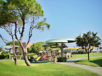 Groene speeltuin met kleurrijke glijbanen en schaduwrijke zitplaatsen in een hoteltuin.