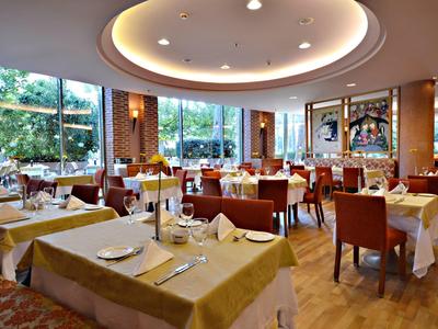 Licht eetzaal met grote ramen, gedekte tafels en comfortabele stoelen.