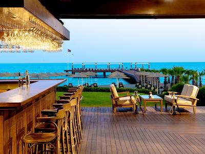 Otevřený plážový bar s dřevěným pultem a posezením s výhledem na oceán a molo.