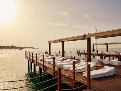Houten steiger met witte ligbedden en zonwering boven water bij zonsondergang