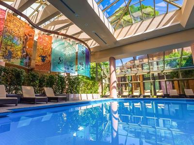 Licht overdekt zwembad met hangmatten en glazen dak waar daglicht doorheen komt.