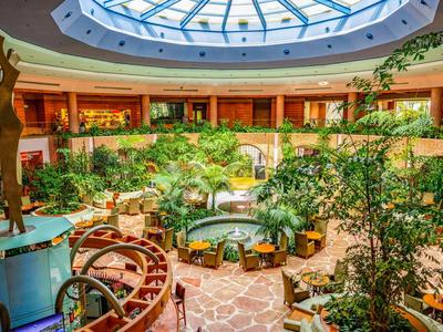 Hotelinterieur met atrium, planten en zitgedeeltes onder een grote koepel.