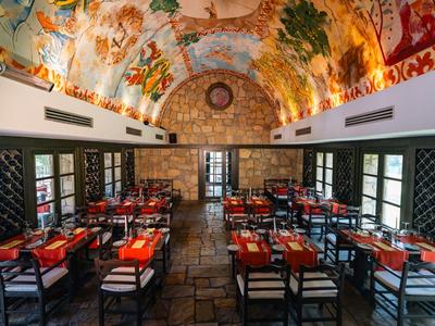 Elegantní restaurace s malovaným stropem, dřevěnými stoly a černými židlemi v hotelu.