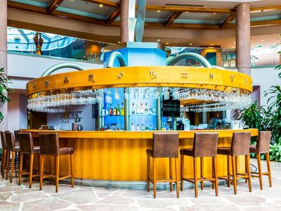 Moderní kulatý bar v hotelu se žlutým pultem a několika barovými židlemi v tropickém prostředí.