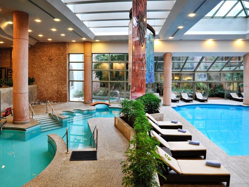 Licht binnenzwembad met ligstoelen en glazen dak in een hotel.