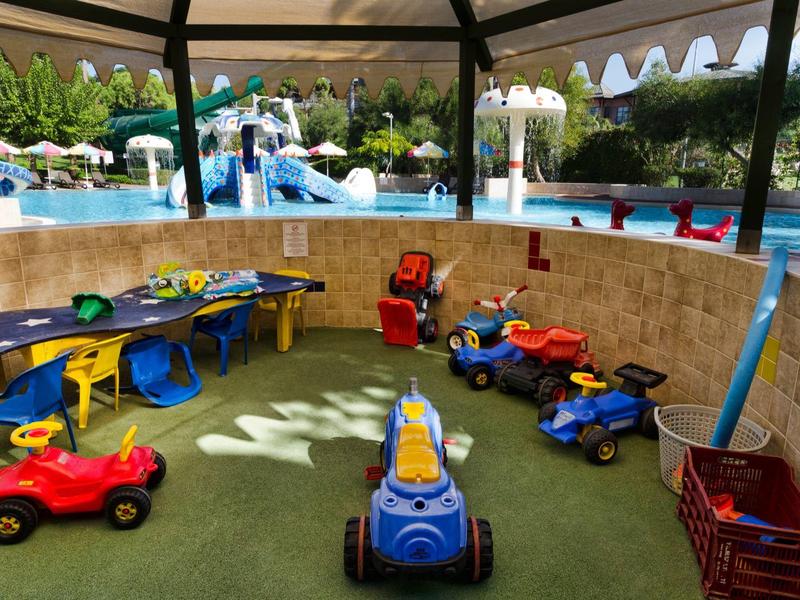 Speelruimte voor kinderen met kleine voertuigen en zitplaatsen naast een zwembad.