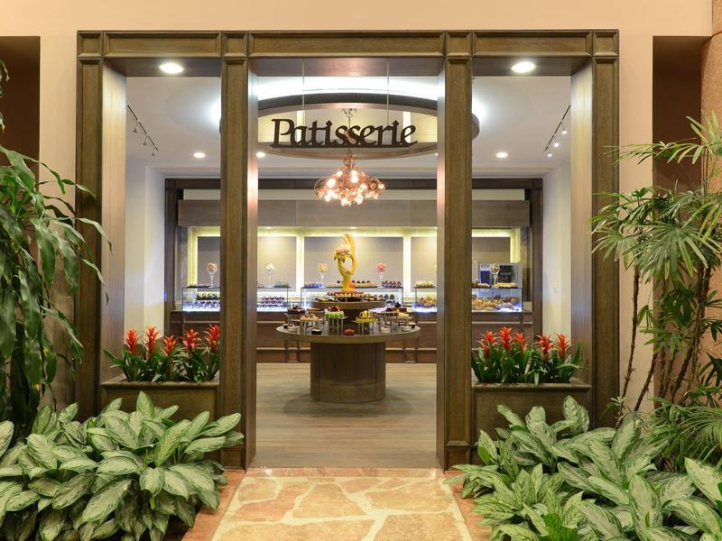 Elegante ingang naar een patisserie met glazen deuren, omgeven door groene planten.