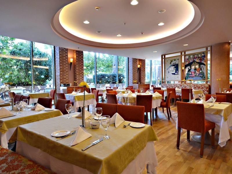 Licht eetzaal met grote ramen, gedekte tafels en comfortabele stoelen.