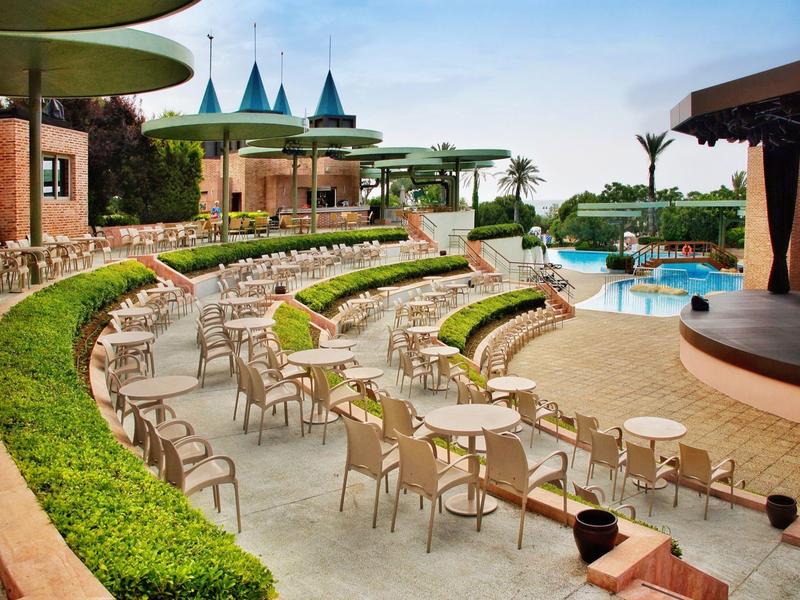 Buitenruimte van hotel met zitplaatsen en uitzicht op zwembad onder blauwe lucht.