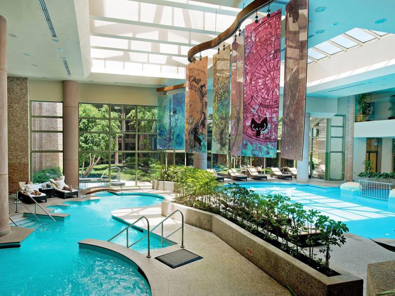 Lichte binnenzwembadruimte met spa, planten en kleurrijke hangdecoraties.