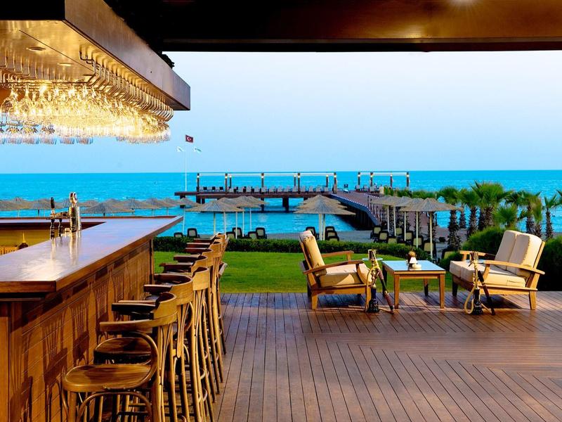 Open bar met houten meubels met uitzicht op zee en een pier bij zonsondergang.