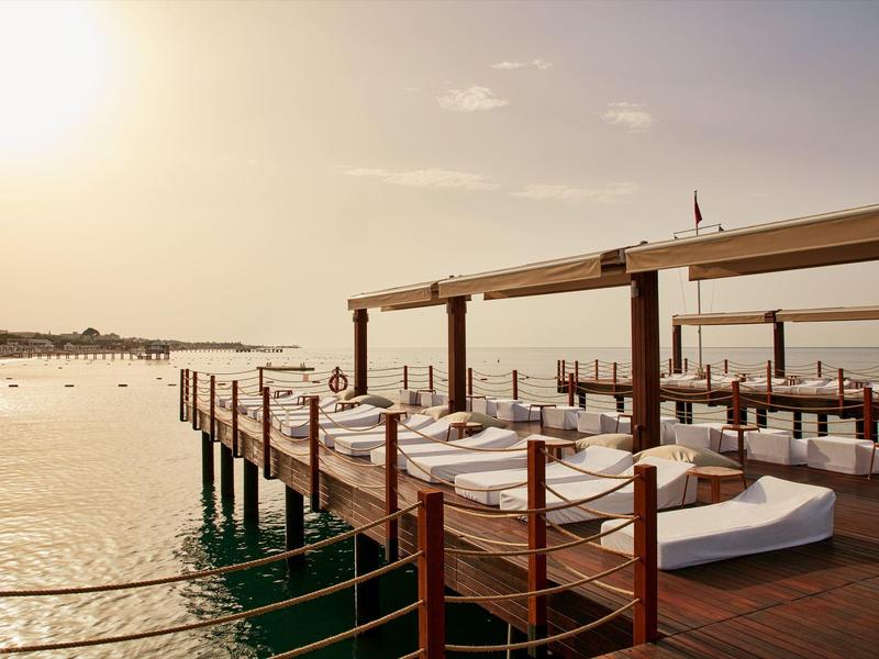 Houten steiger met witte ligbedden en zonwering boven water bij zonsondergang