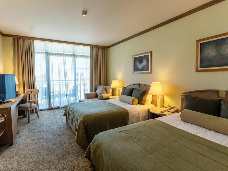 Hotelkamer met drie bedden, bureau, tv en balkonramen met gordijnen.