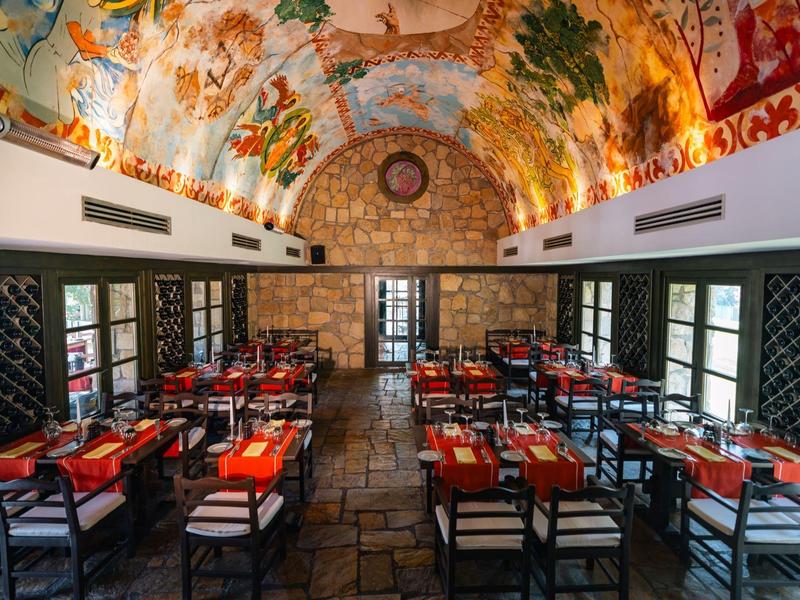 Een stijlvol restaurant met een beschilderd plafond, houten stoelen en tafels met rode tafelkleedjes.