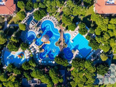 Widok z lotu ptaka na duży hotel z kilkoma niebieskimi basenami otoczonymi gęstą zielenią.