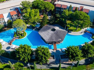 Großer Pool mit Insel und Sonnenschirm, umgeben von Hotelgebäuden und Bäumen.
