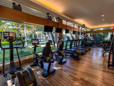 Moderner Fitnessraum mit Holzboden und großen Fenstern mit Blick auf Garten und Palmen.