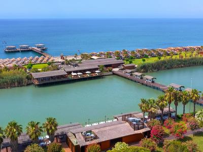 Resort mit Wasservillen, Pool und Palmen an einem tropischen Strand.