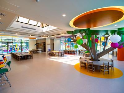 Helles Hotelrestaurant mit großem Baumdekor und vielen Sitzgelegenheiten unter natürlichem Licht.