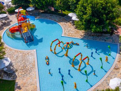 Kinderplanschbecken mit bunten Wasserspielen in einer Hotelanlage umgeben von Liegestühlen und Bäumen.