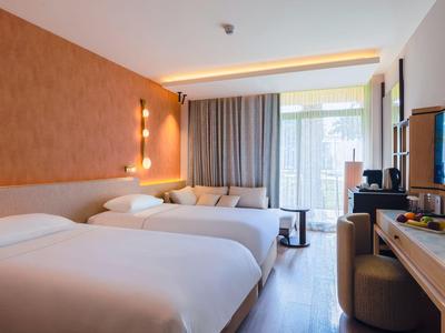 Heller Hotelzimmer mit zwei bequemen Betten, modernem Mobiliar und Balkon mit Vorhängen.
