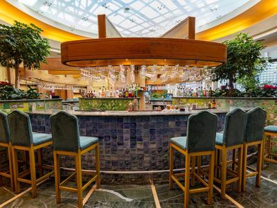 Moderne Bar in hellem Innenraum mit Holzstühlen und großer Deckenverglasung.