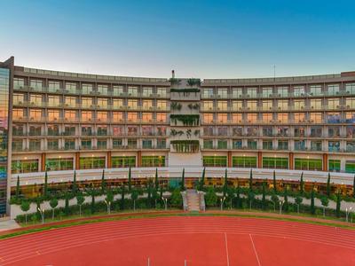 Modernes Hotelgebäude mit mehreren Balkonen und großem rotem Sportplatz im Vordergrund.