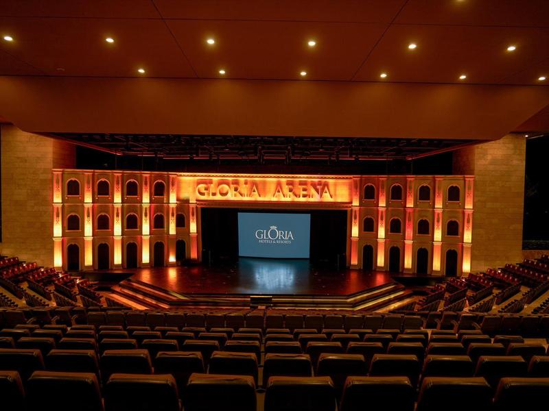 Wnętrze teatru z oświetloną sceną i rzędami siedzeń na pierwszym planie.