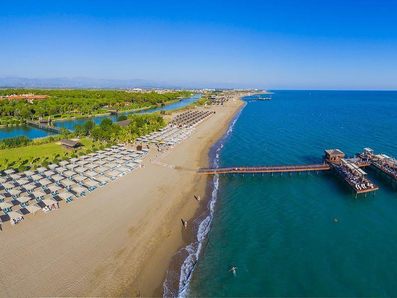 Długa piaszczysta plaża z rzędami parasoli i molo sięgającym w niebieskie morze.