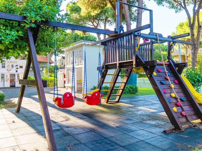 Kolorowa huśtawka dla dzieci ze ścianką wspinaczkową na słonecznym placu zabaw obok drzew.