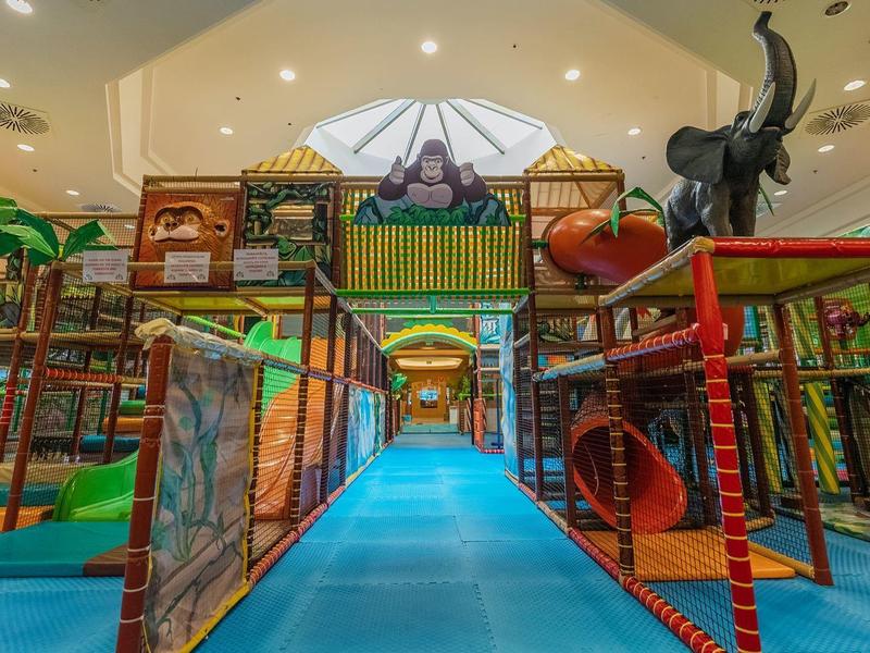 Jasna, kolorowa kryta konstrukcja placu zabaw dla dzieci z zjeżdżalniami i siatkami do wspinaczki pod białym dachem.