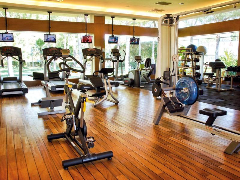 Nowoczesna siłownia z bieżniami, rowerami i wioślarzami na drewnianej podłodze.
