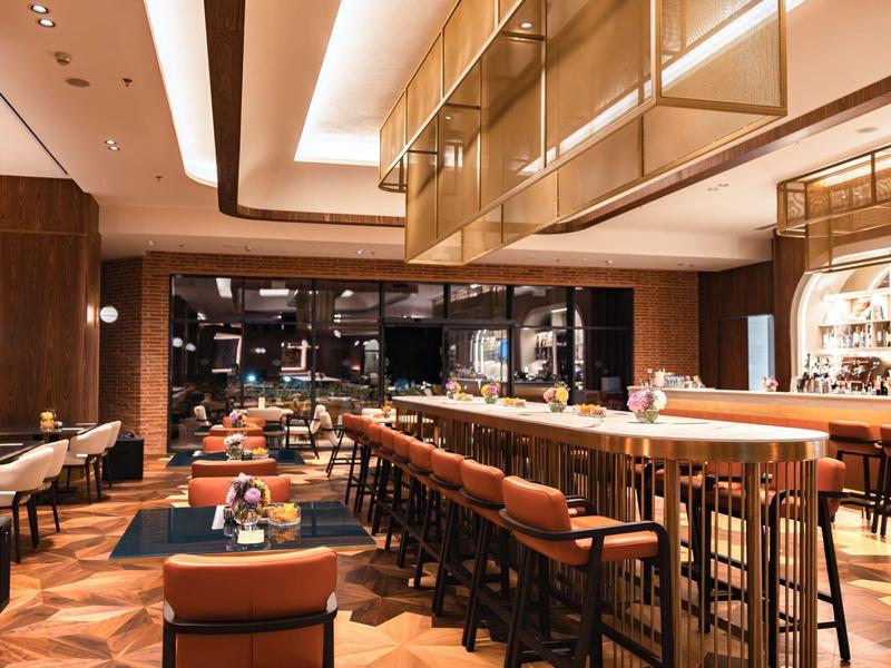 Nowoczesny bar hotelowy z długimi rzędami siedzeń, ciepłą drewnianą podłogą i stylowym oświetleniem.