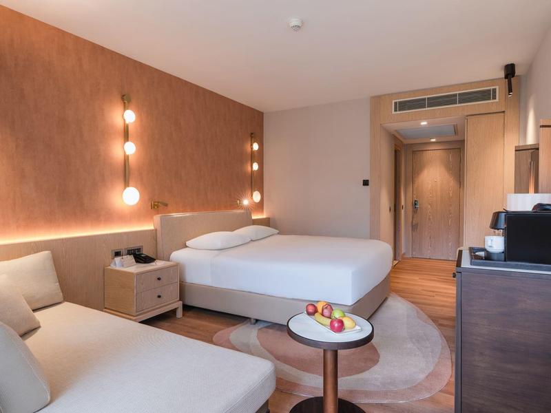 Nowoczesny pokój hotelowy z łóżkiem podwójnym, częścią wypoczynkową, stolikiem nocnym i telewizorem.